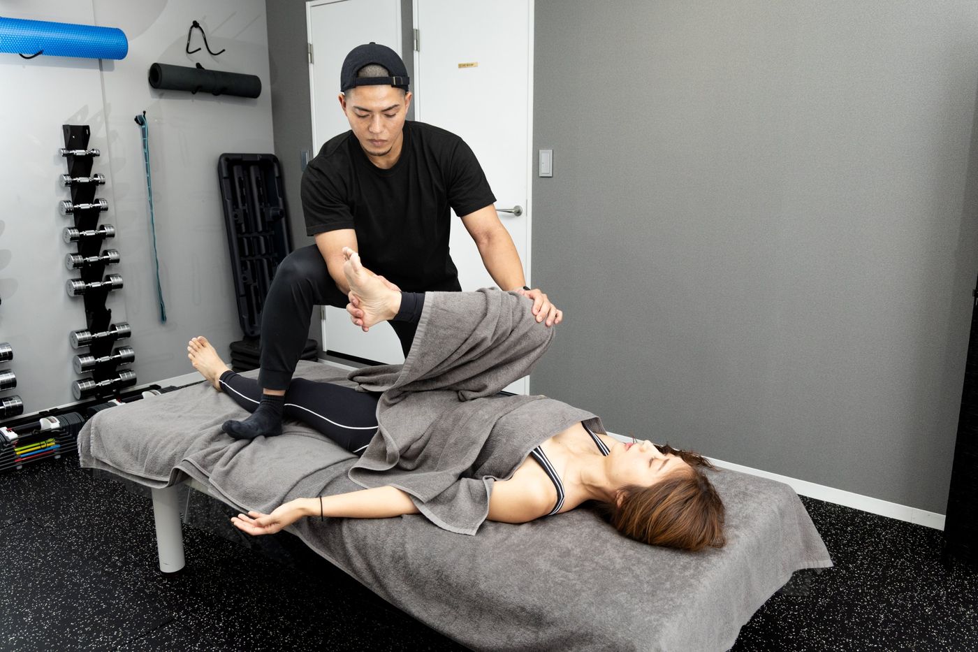 ベッドの上で、トレーナーと一緒に脚のストレッチをする女性